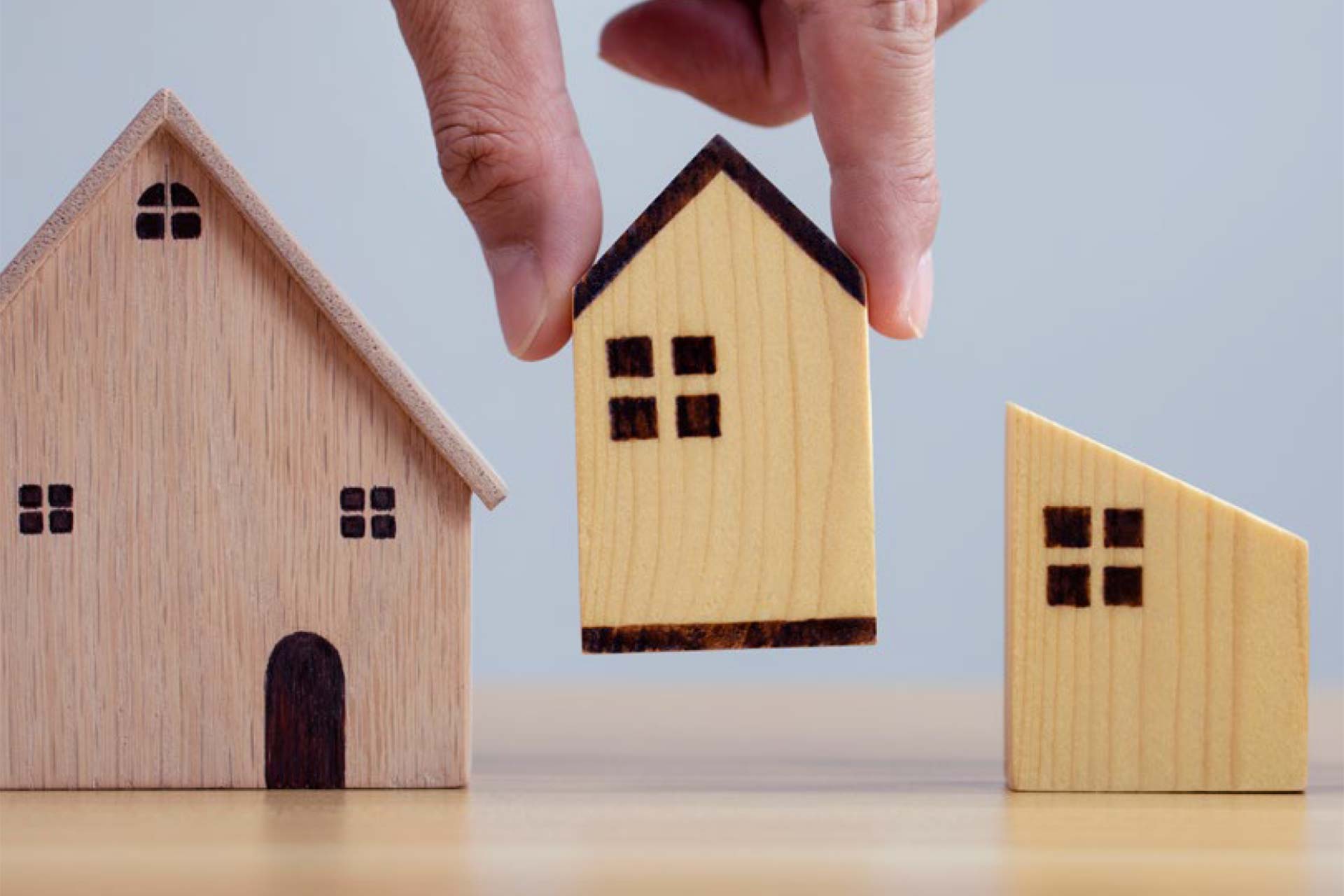 Hand picking up little wooden house. 3 houses in a row