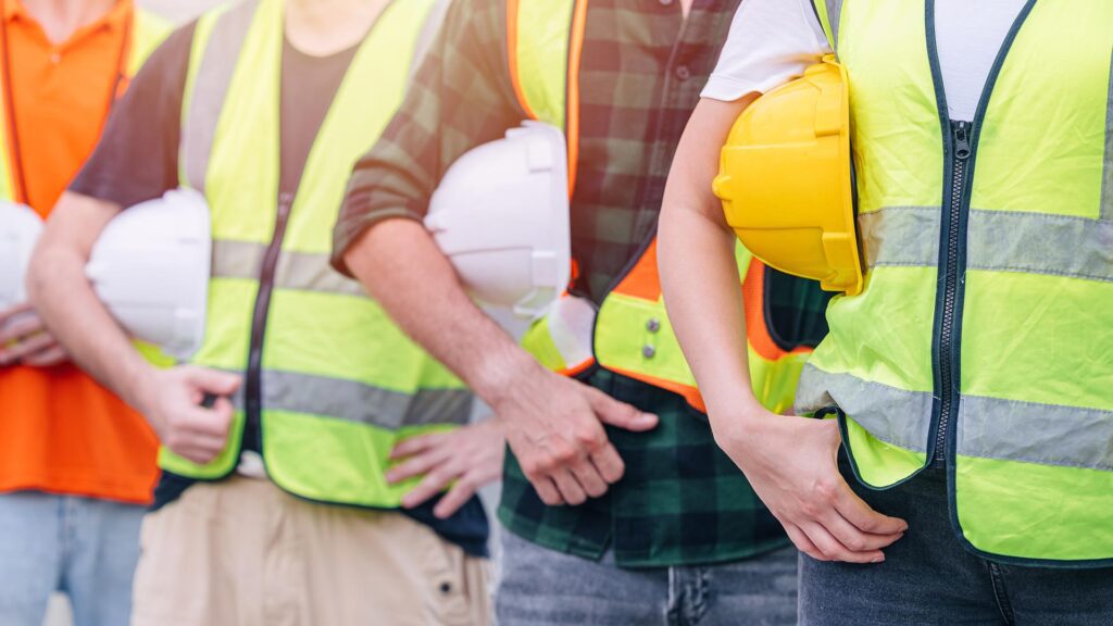 Close up of row of people in high vis holding helmets