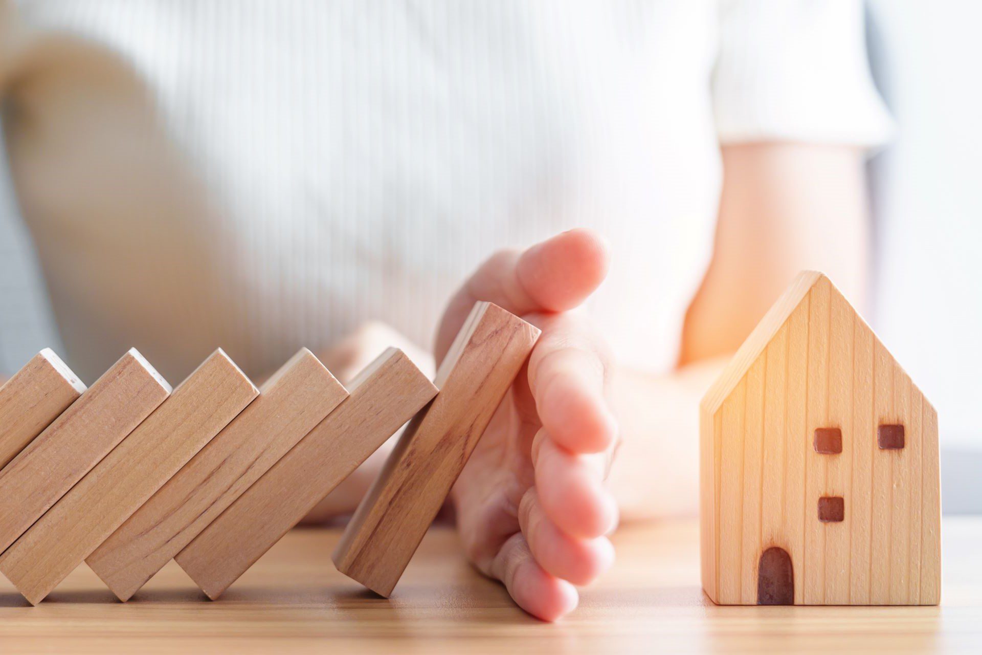 Hand stopping wooden dominoes falling on wooden house